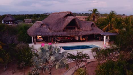 Drone-shot-slow-pull-away-and-reveal-luxury-villa-with-Palapa-and-large-pool-at-sunset-in-Oaxaca-Mexico