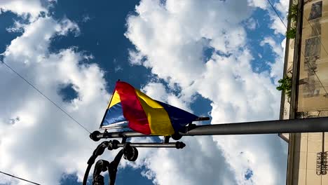 Bandera-Rumana-Vertical-En-La-Lámpara-De-La-Calle-De-La-Ciudad-Soplada-Por-El-Viento,-ángulo-Bajo