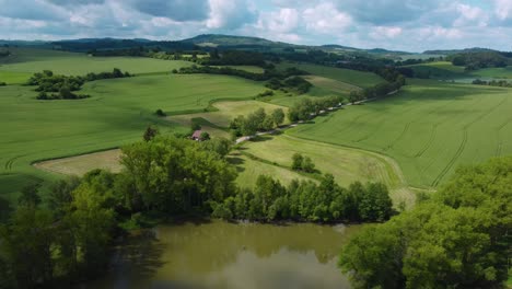 Luftaufnahme-Einer-Ruhigen-Grünen-Landschaft-Mit-Feldern,-Grüner-Vegetation-Und-Einem-Teich