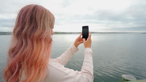 Smiling-woman-with-pink-hair-on-the-coast-of-eastern-Canada-taking-a-phone-on-her-cell-phone-during-midday