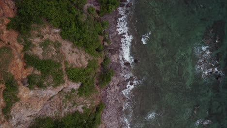 Top-aerial-view-on-a-rocky-cliff-with-trees-and-waves-on-the-island-of-Koh-Larn-in-Thailand
