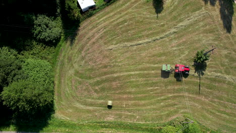 Tractor-with-hay-rolling-equipment-gathering-heaps-of-straw-hay-and-roles-in-bales---aerial-top-down-view