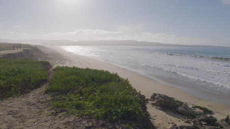 Slow-motion-shot-of-a-sunny-day-at-California-Monterey-Bay-Marina-State-Beach-with-people-on-the-edge-of-the-cliff