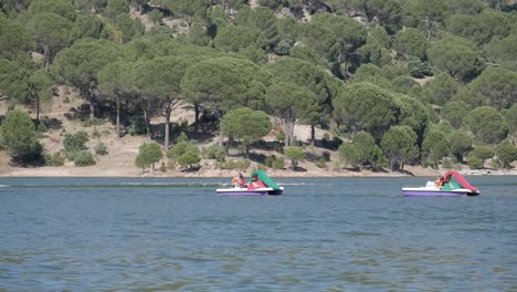 Two-pedalo-or-paddle-boats-on-lake-as-motor-boat-passes-behind
