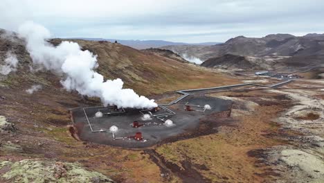 Vista-Aérea-De-Pozos-De-Alta-Temperatura-Y-Humo-Saliendo-De-Una-Tubería-En-Una-Estación-De-Energía-Geotérmica-En-Islandia