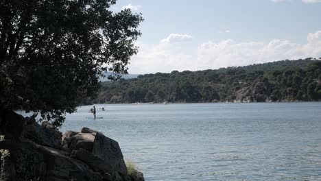 Beautiful-lake-scenery-with-people-enjoying-watersports,-kayak-and-standup-paddleboarding,-at-reservoir-pantano-de-San-Juan-,-Madrid