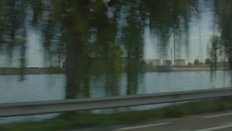 Driving-past-large-industrial-terrain-located-next-to-a-river---View-from-car-window