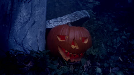 Halloween-pumpkin-by-tombstone,-flashing-light-and-fog,-horror-atmosphere,-slider-closeup-shot