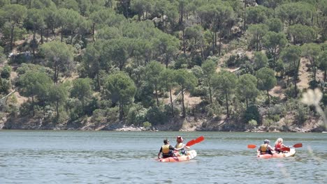 Dos-Kayaks-Con-Dos-Personas-Cada-Uno-Remando-En-Un-Día-De-Verano-A-Través-De-Las-Aguas-Dulces-Del-Embalse-En-El-Pantano-De-San-Juan,-Madrid