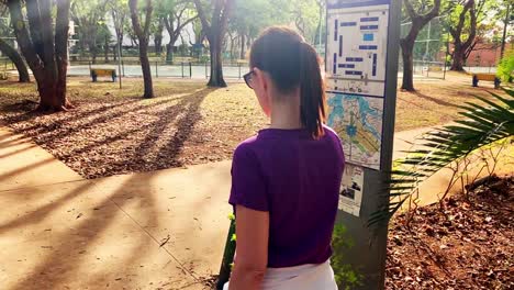 Rear-view-of-young-female-with-ponytail-leisurely-walking-through-a-park-in-a-city
