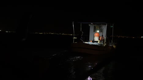 Ein-Kleines-Beleuchtetes-Fischerboot-Flacht-Nachts-Auf-Dem-Offenen-Wasser-Ab