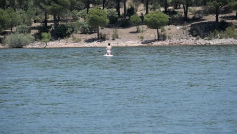 Woman-on-knees-paddling-on-top-of-stand-up-paddle-board-at-lake,-pantano-de-San-Juan,-Madrid