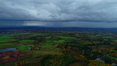 Aerial-flyover-green-landscape-with-forest-and-lake-during-dark-cloudy-day