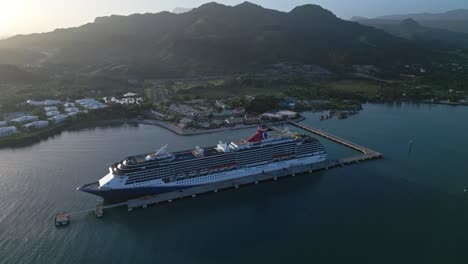 Aerial-drone-shot-of-docking-large-cruise-ship-at-port-of-Puerto-Plata-during-sunset,-Dominican-Republic
