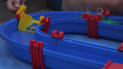 Hand,-Die-Gelben-Aufzug-Auf-Blauem-Wasserspielspielzeugsatz-Dreht