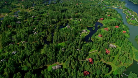 Aerial-drone-forward-moving-shot-over-cottages-beside-small-lakes-surrounded-by-lush-green-vegetation-at-daytime