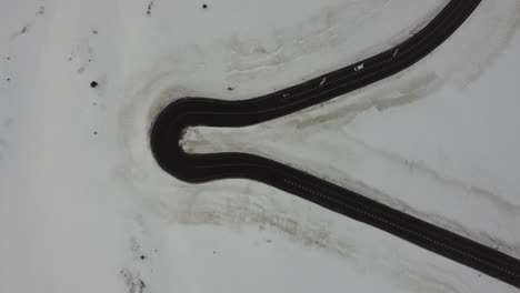 Top-down-aerial-view-of-white-car-driving-sharp-road-turn-against-snow-landscape