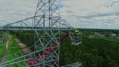 Two-workers-on-a-crane-fixing-a-high-voltage-tower-in-a-wooded-setting