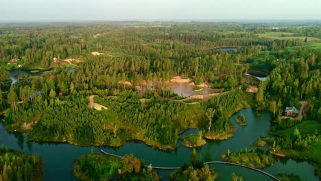 Aerial-drone-shot-over-picturesque-calm-lakes-surrounded-by-green-coniferous-trees-at-sunrise