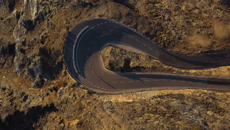 Top-down-aerial-view-of-fast-cyclist-taking-sharp-road-turn-in-remote-landscape