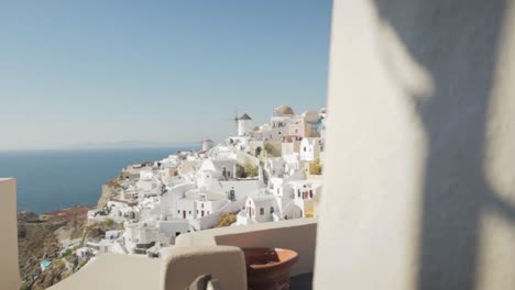 Wide-pan-reveal-of-white-traditional-windmills-and-greek-flag-in-Santorini,-Greece