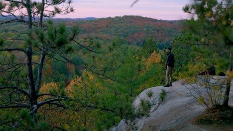 Hiker-stands-at-edge-of-cliff-and-looks-out-over-scenic-Fall-landscape