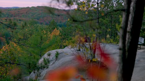 Hiker-walks-out-to-edge-of-cliff-lookout-point-in-scenic-fall-landscape