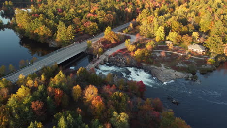Colorful-Autumn-Forest-by-Mountain-River-and-Highway-Road,-aerial-view-Muskoka-Region-of-Ontario,-Canada