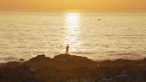 Silhouette-Eines-Fischers,-Der-Bei-Sonnenaufgang-Im-Ozean-Fischt
