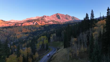 Bergbeleuchtete-Gipfel-Und-Ein-Luftstrom,-Der-An-Einem-Epischen-Frühen-Morgen-In-Colorado-Eine-Unbefestigte-Straße-Hinunterrollt