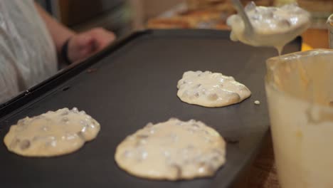 Woman-places-chocolate-chip-pancake-batter-onto-heated-pan-in-slow-motion