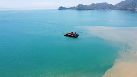 Aerial-drone-of-ocean-oil,-gas-offshore-platform-rig-in-the-shallows-of-capital-Dili,-Timor-Leste-in-Southeast-Asia,-popular-tourist-destination-of-Cristo-Rei-statue-in-the-distance