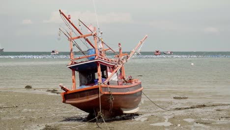 A-tilt-down-reveal-shot-of-a-moored-beached-Squid-fishing-boat-during-low-tide-in-Thailand