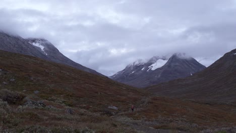 Far-view-of-person-hiking-during-moody-morning-in-valley-between-wild-mountains-in-Norway