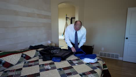 Executive-older-man-using-packing-cubes-to-organize-items-in-his-luggage-for-a-business-trip