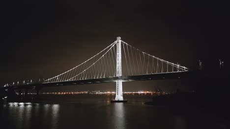 Bay-Bridge-at-night-low-angle-over-water-with-Oakland-in-background-as-cars-commute,-San-Francisco-California