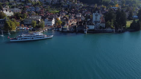 Fantástica-Toma-Aérea-Sobre-El-Castillo-De-Oberhofen-Y-Donde-Se-Puede-Ver-La-Costa-Y-Un-Barco-Acercándose-Al-Muelle,-En-Suiza-En-Un-Día-Soleado