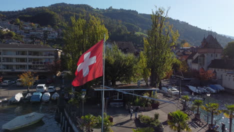 Fantástica-Toma-Aérea-En-órbita-De-La-Bandera-Suiza,-Toma-Realizada-En-El-Municipio-De-Oberhofen-En-Suiza,-En-Un-Día-Soleado