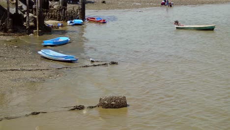 Eine-Einspielung-Kleiner-Blauer-Plastikboote,-Die-Bei-Ebbe-Im-Seichten-Wasser-In-Einem-Traditionellen-Fischerdorf-In-Si-Racha,-Thailand,-Festgemacht-Sind