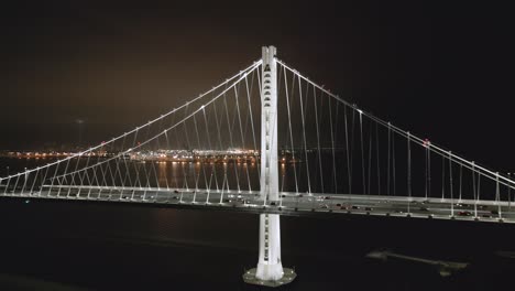 Aerial-Shot-of-Bay-Bridge-at-night-pulling-back-with-Oakland-in-background-as-cars-commute,-San-Francisco-California