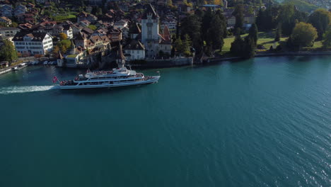 -aerial-shot-of-tracking-over-a-passenger-ship-and-seeing-the-castle-of-Oberhofen-in-switzerland,-on-a-sunny-day