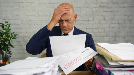 A-stressed-man-with-headache-opening-a-stack-of-bills-and-letters-with-final-notice-for-credit-card-debts