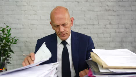 An-over-worked-and-overwhelmed-businessman-at-work-with-stacks-of-paperwork-on-his-desk