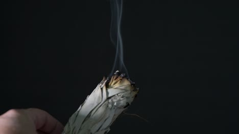 Burning-sage-in-a-shell-on-a-wood-table-with-black-background-showing-sage-smoke