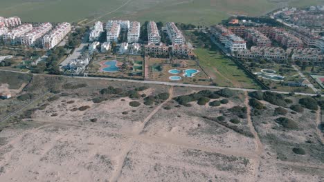 drone-view-of-the-mountain-with-mills-and-urbanization-on-the-beachfront-in-the-beautiful-beach-of-CADIZ-with-white-sand-and-waves-for-surfing
