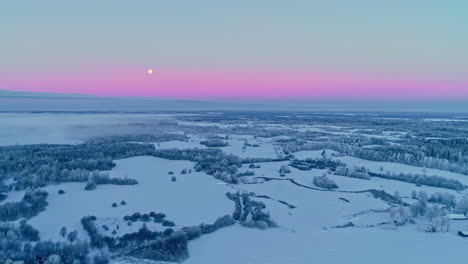 Aerial-flyover-snowy-rural-fields-during-purple-colored-sky-with-full-moon-at-horizon-in-winter