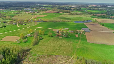 Cinematic-drone-backward-moving-shot-capturing-beautiful-green-farmlands-along-with-village-cottages-at-daytime