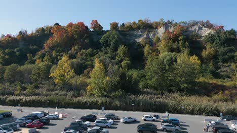 Drone-shot-of-a-parking-lot,-we-fly-up-to-a-hill-filled-with-trees-with-fall-colors