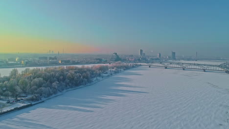 Riga,-Lettland-Im-Winter-über-Dem-Zugefrorenen-Fluss-Daugava-Und-Brücken,-4k-drohnenansicht
