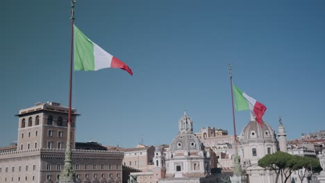 Banderas-Italianas-Ondeando-Con-El-Viento-En-El-Altar-De-La-Patria-Con-La-Columna-De-Trajano-E-Iglesias-Católicas-En-Piazza-Venezia,-Roma,-Italia